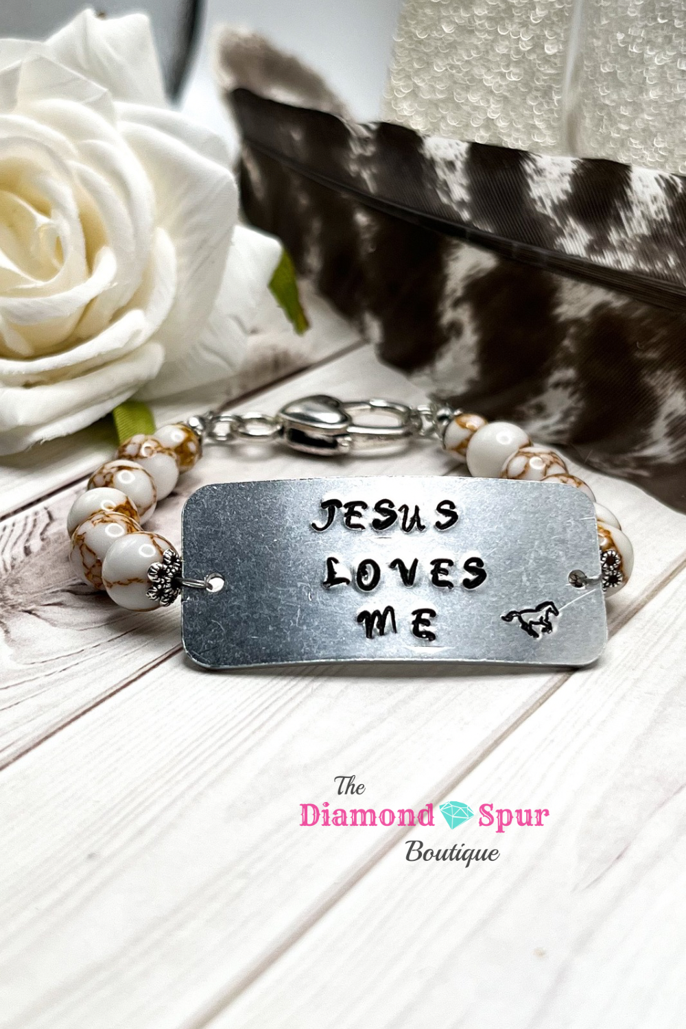 Metal stamped bracelet that says Jesus Loves Me and has white and gold beads