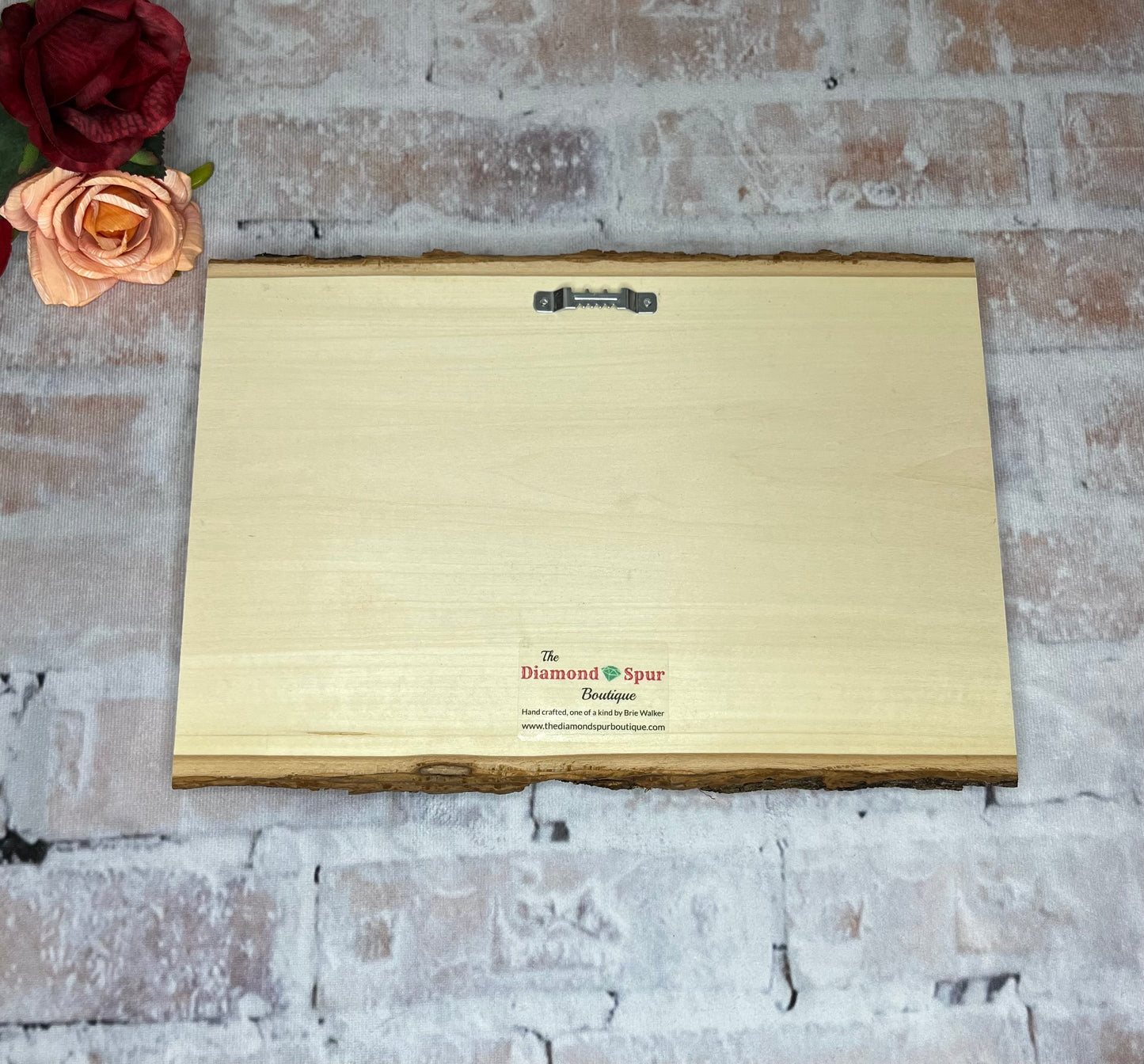 The back of a natural wood plaque with metal sawtooth hanger and boutique logo